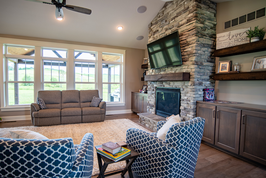 Living room with stone fireplace, and 4 large double-hung windows. A couch is placed in front of the windows.