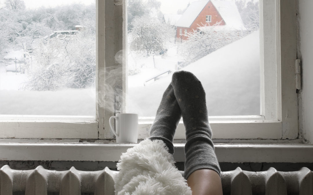 A woman has warm socks on with her feet by the winter window and a cup of coffee. Her windows are ready for winter